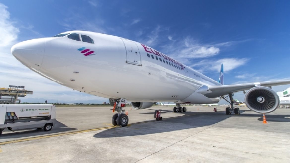 Ein großes weißes Flugzeug einer Fluggesellschaft, das auf dem Rollfeld eines Flughafens unter einem strahlend blauen Himmel geparkt ist.