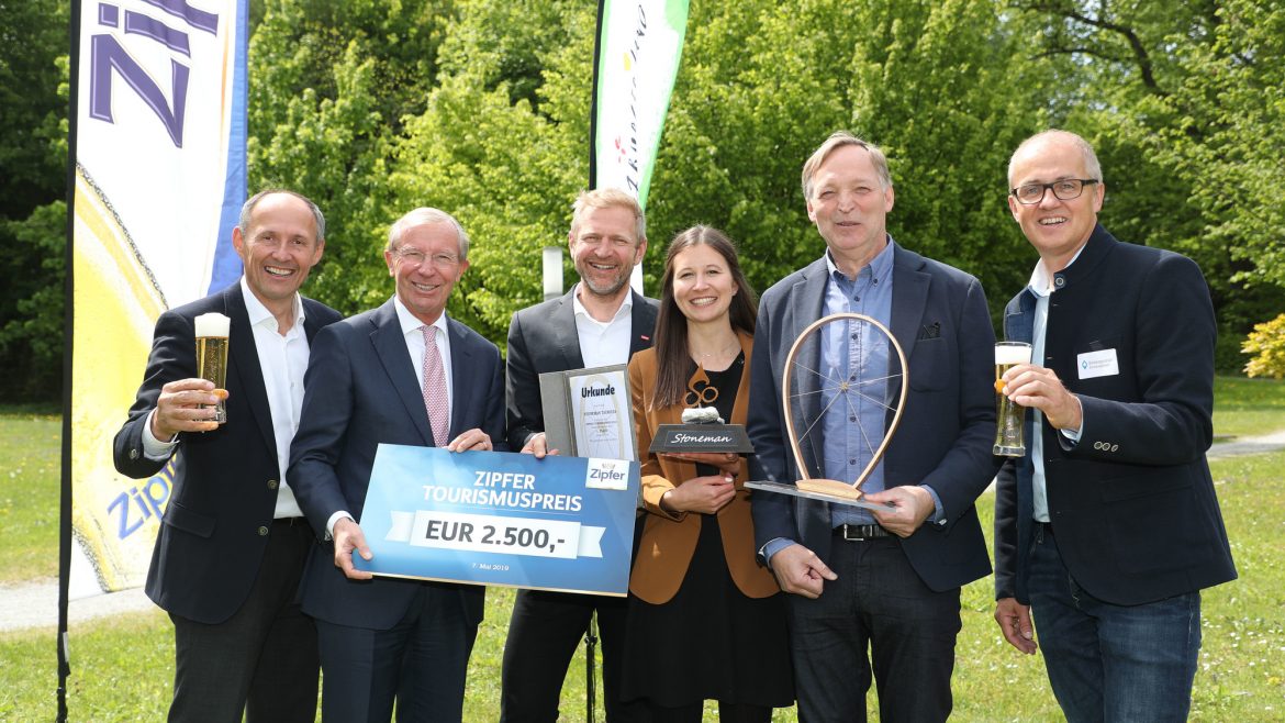 Sechs lächelnde Menschen halten eine Trophäe, ein Preisschild und Getränke bei einer Veranstaltung zur Verleihung des Outdoor-Tourismuspreises.