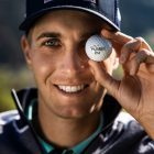 Ein lächelnder Mann mit einer Red-Bull-Mütze hält einen Golfball mit der Aufschrift Salzburger Land an sein rechtes Auge.