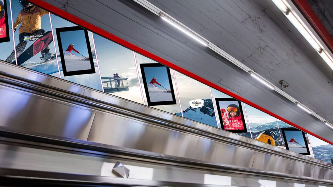 Ski- und Snowboardposter säumen die Wand über einer Rolltreppe in einer Halle.