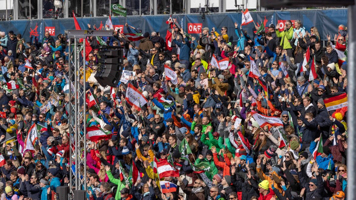 Eine große Menge jubelnder Fans, die bei einem Sportereignis im Freien Fahnen und Transparente halten.
