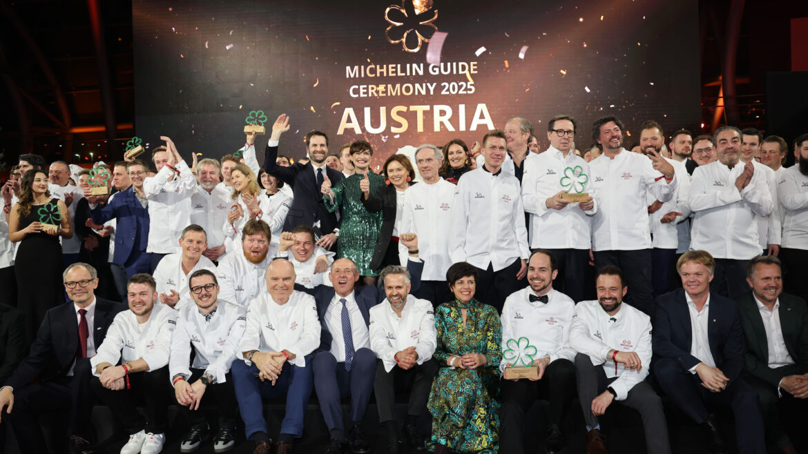 Eine große Gruppe von Köchen in weißen Jacken posiert auf der Bühne bei der Verleihung des Michelin-Führers Österreich 2025.