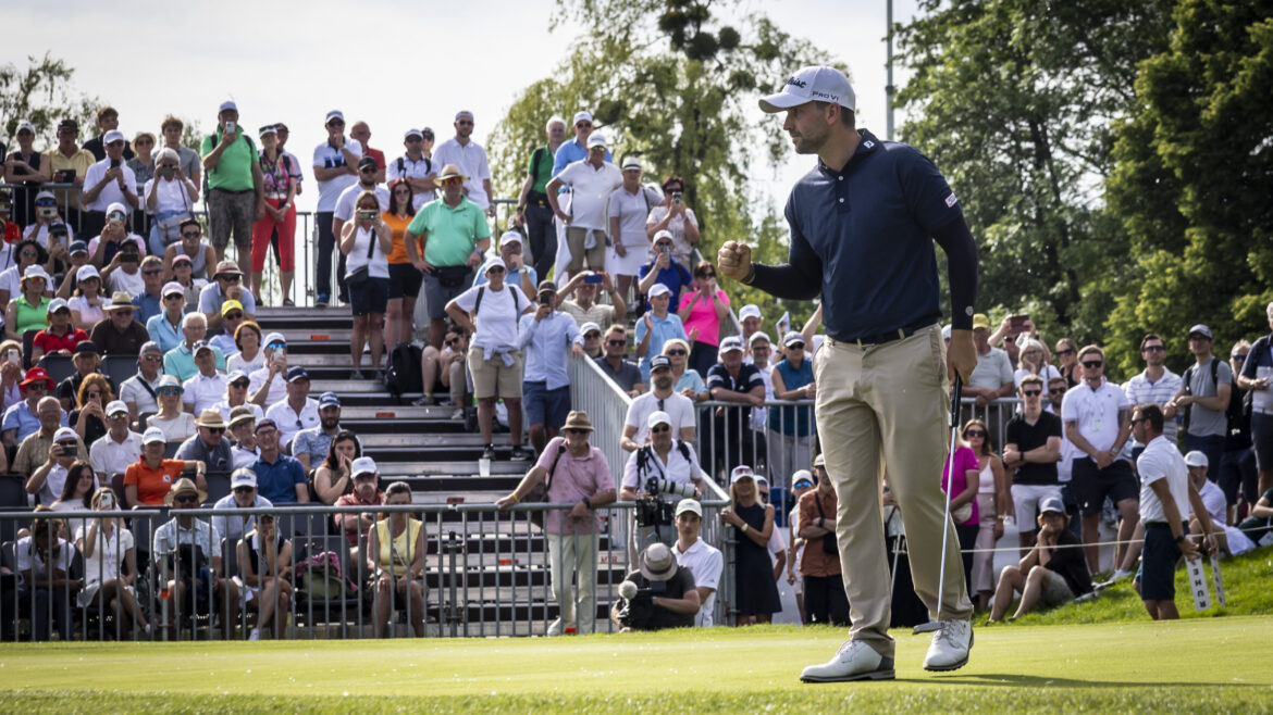 Ein Golfer jubelt auf dem Grün, während eine große Menschenmenge bei einem Golfturnier im Freien zusieht.