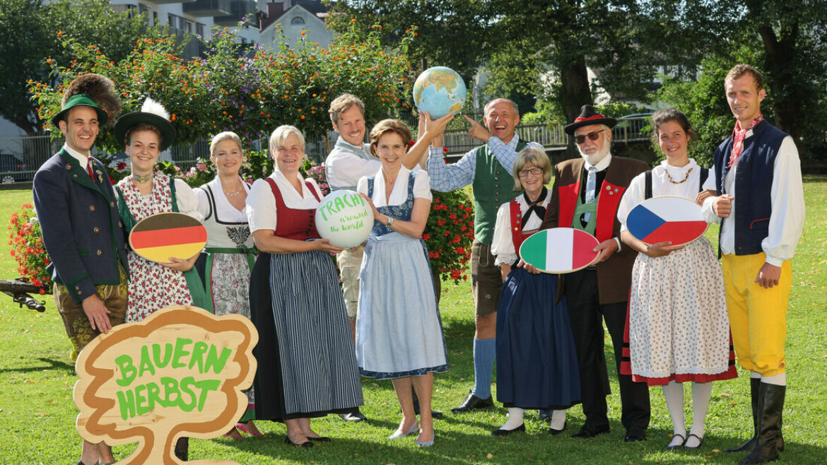 Eine Gruppe in traditioneller österreichischer Tracht posiert im Freien und hält Landesschilder und ein Bauernherbst-Schild.