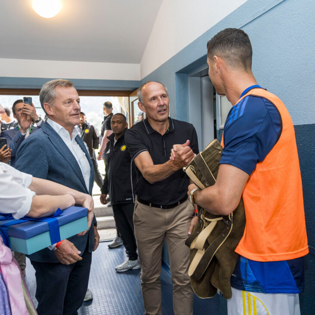 Ein Mann in Sportkleidung erhält einen Händedruck und Geschenke von Menschen, darunter eine Frau in traditioneller Kleidung.