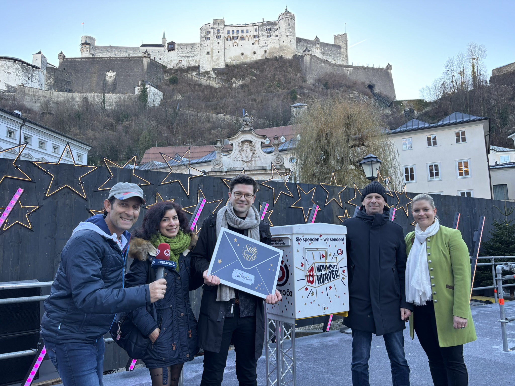 Fünf Personen posieren im Freien in Winterkleidung mit einer Burg auf einem Hügel im Hintergrund.