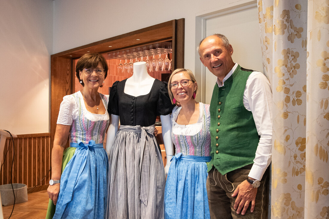 Drei Personen in traditioneller österreichischer Tracht stehen in einem Raum neben einer Schaufensterpuppe, die ein Dirndl trägt.