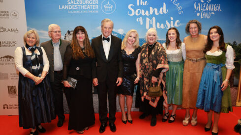 Neun verkleidete Personen posieren gemeinsam auf einem roten Teppich bei der Veranstaltung zum 60. Jubiläum von The Sound of Music.
