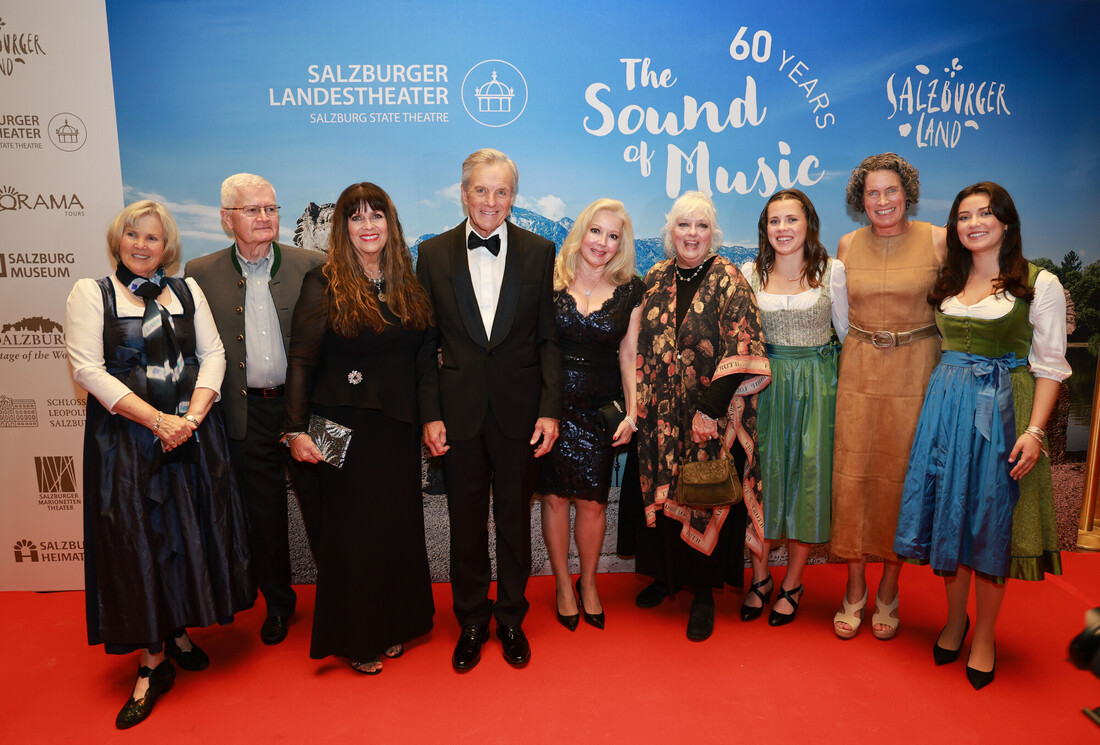 Neun verkleidete Personen posieren gemeinsam auf einem roten Teppich bei der Veranstaltung zum 60. Jubiläum von The Sound of Music.