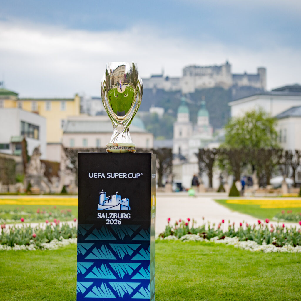 Der UEFA-Supercup-Pokal, ausgestellt in einem Garten mit dem „Salzburg 2026“-Logo und einer Burg im Hintergrund.
